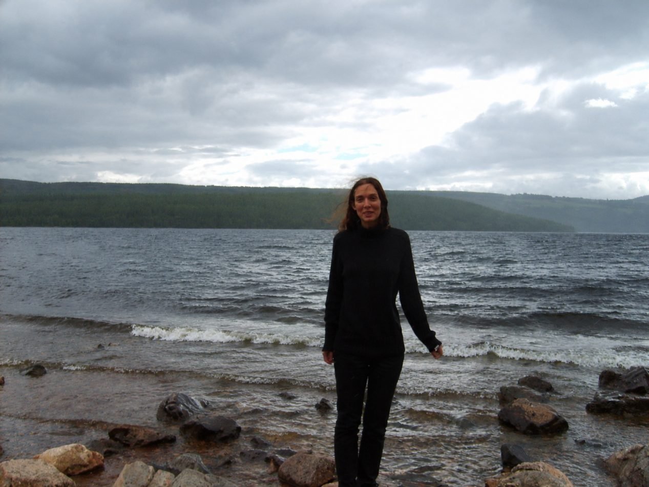 Angélique Olivia standing on the rocky shore of Loch Ness under a grey sky
