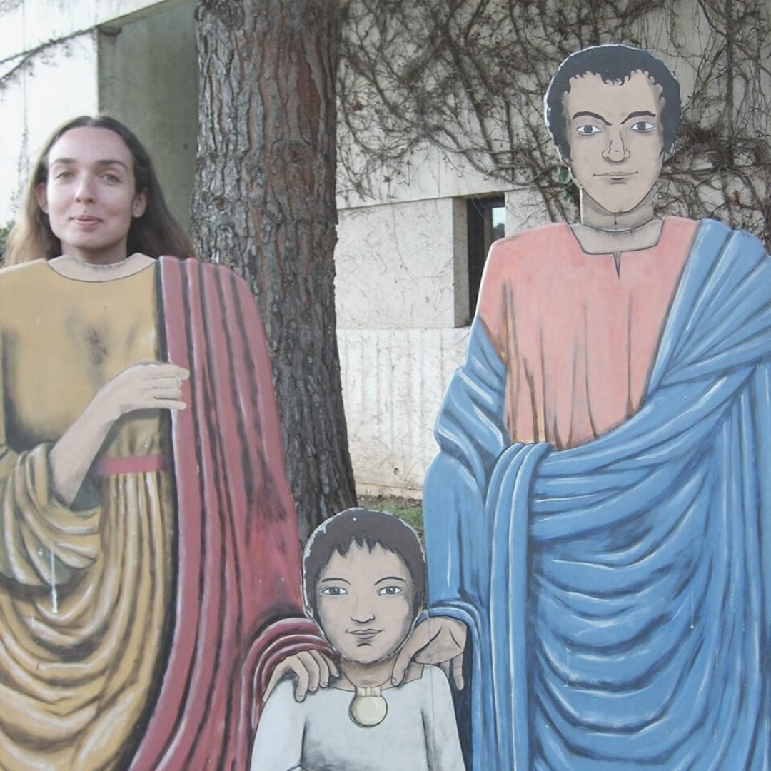 Angélique Olivia posing behind a painted cut-out of a Roman family in Nice