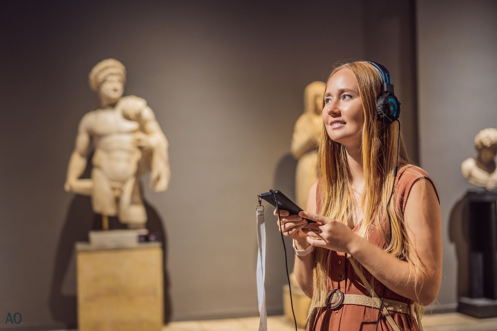 Young woman listening to an audio guide in front of classical sculptures at a museum exhibition